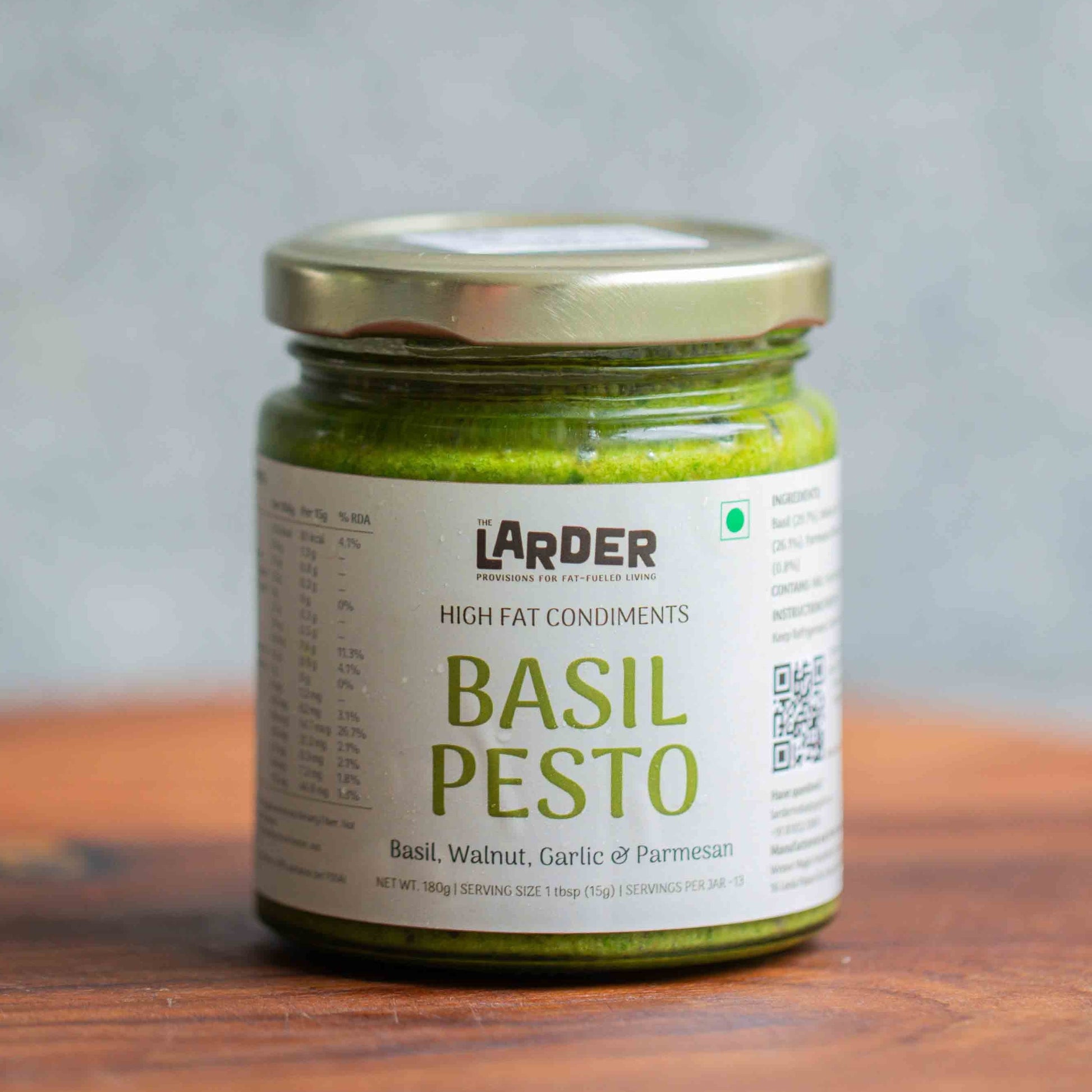 Jar of Larder Basil Pesto on a wooden surface with a gray background