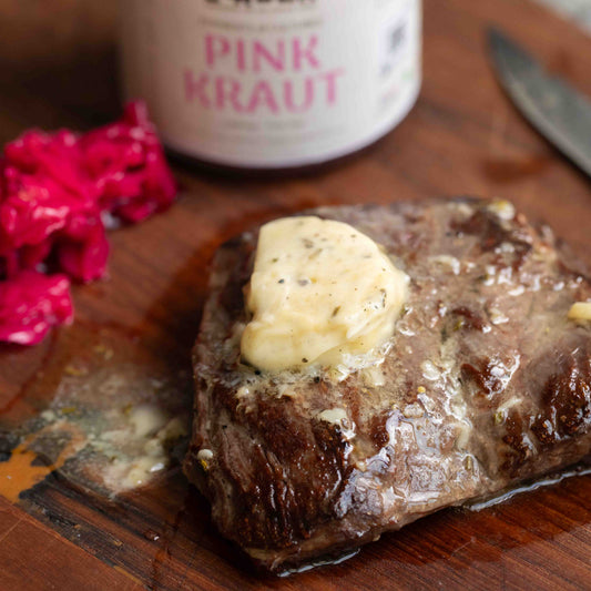 Steak with butter on a wooden cutting board next to pink kraut and a knife.