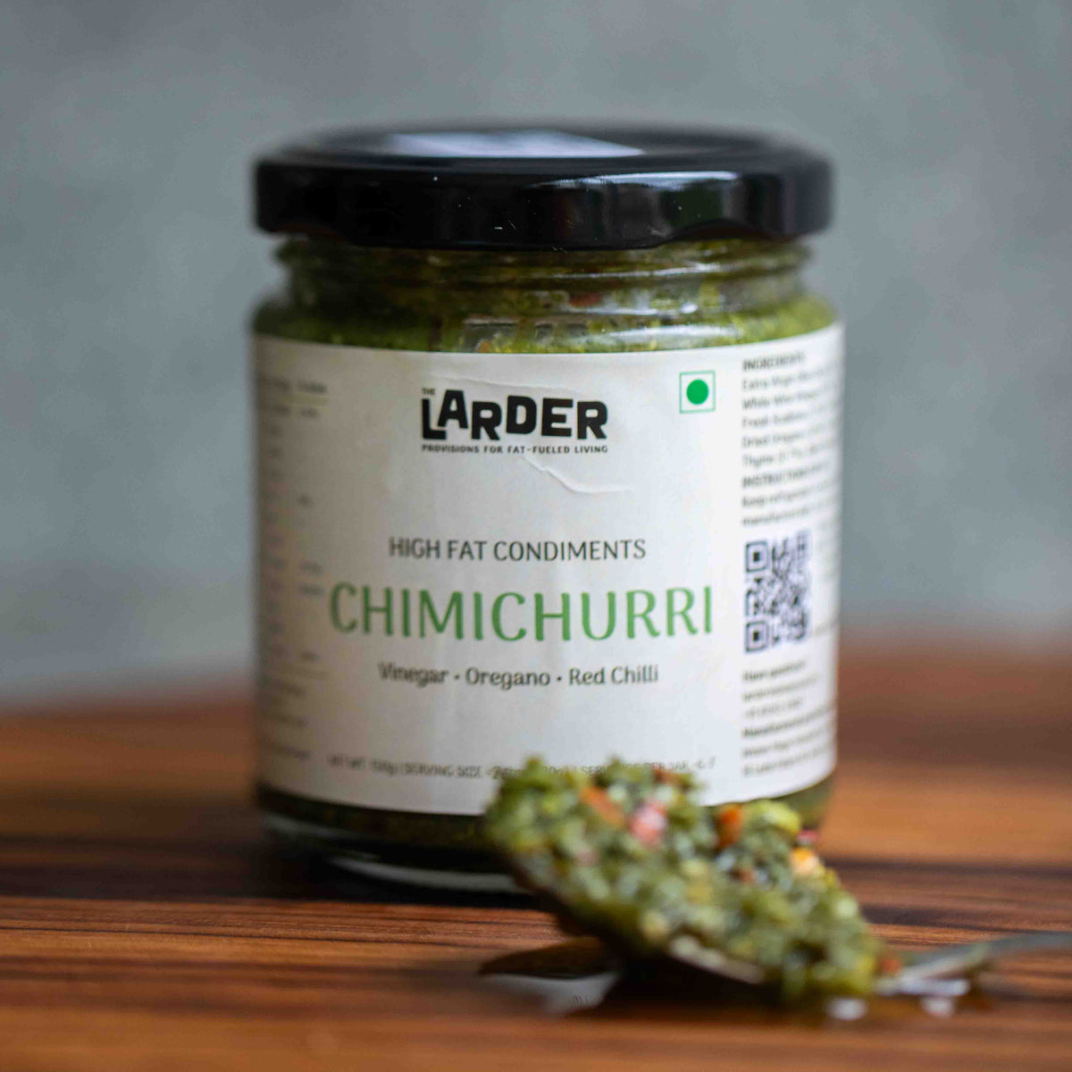 Jar of Larder Chimichurri on a wooden surface with a blurred background