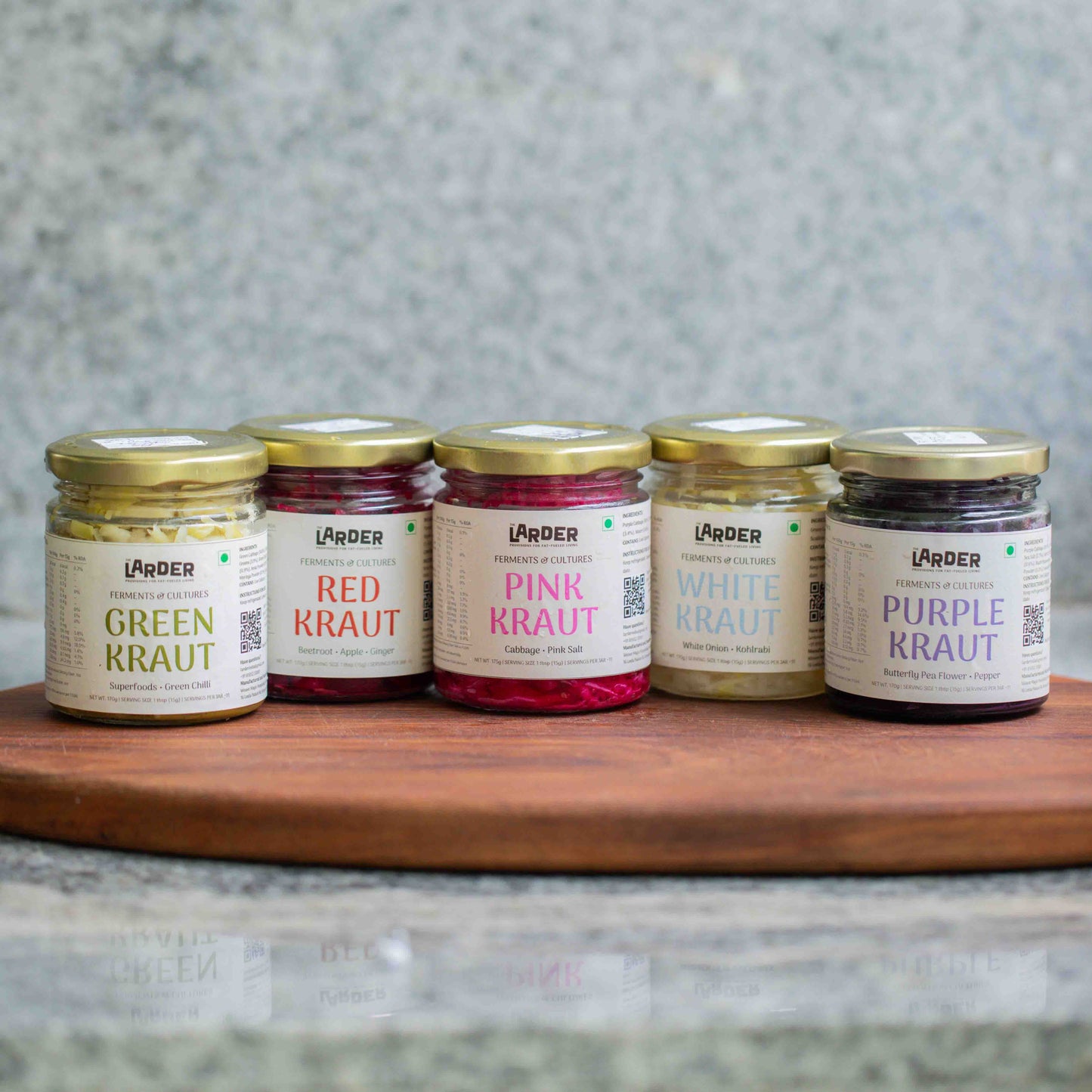 Five jars of different types of gut-friendly lacto-fermentred sauerkrauts on a wooden board with a gray background made at the Larder in Bangalore