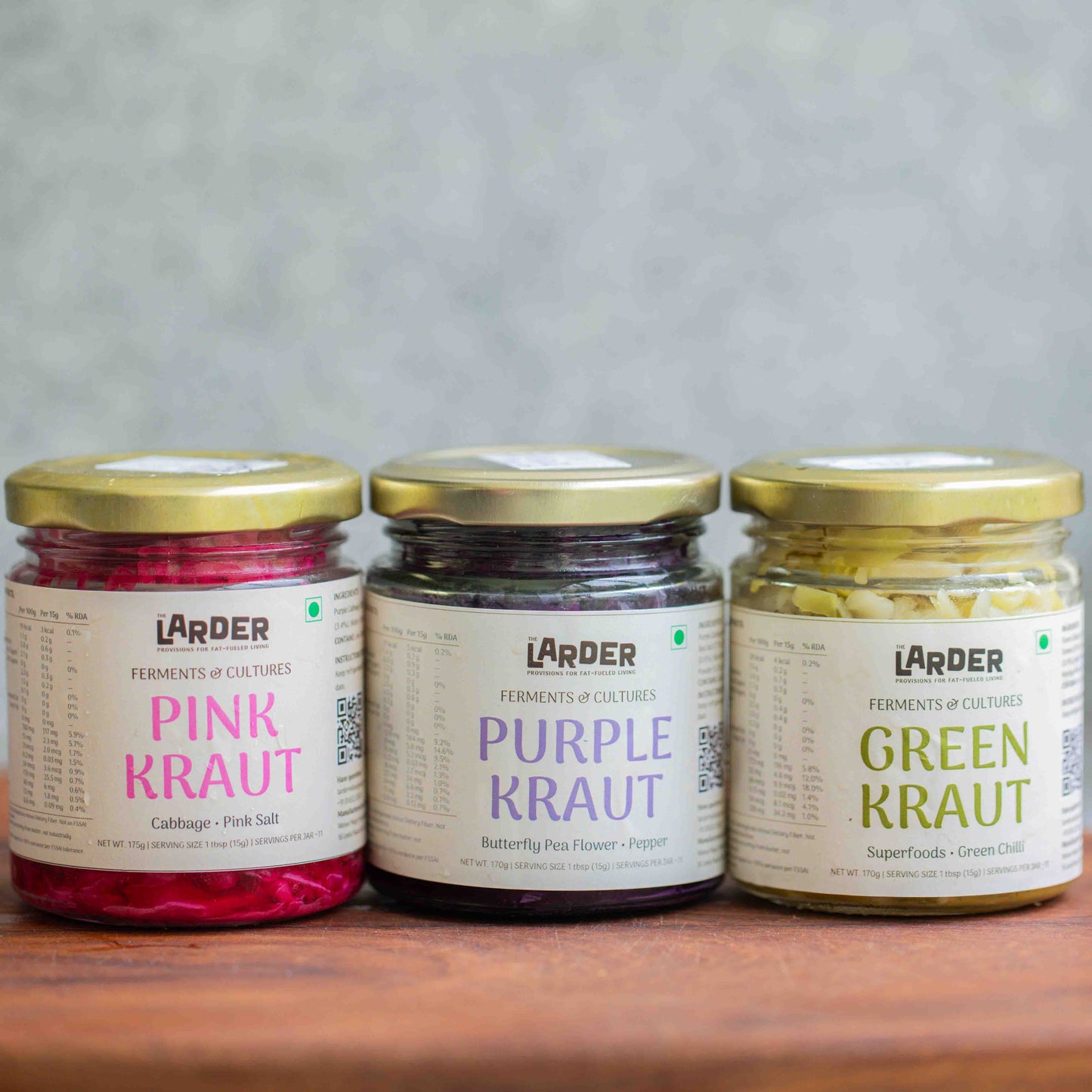 Three jars of Larder kraut on a wooden surface with a gray background